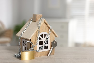 Photo of Home security. House model with chain, key and padlock on wooden table indoors, closeup. Space for text