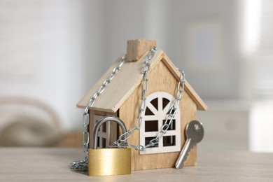 Photo of Home security. House model with chain, key and padlock on wooden table indoors, closeup