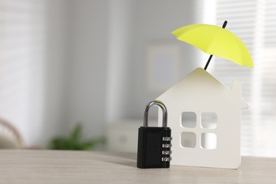 Photo of Home security. House model with small umbrella and padlock on wooden table indoors, closeup. Space for text