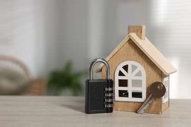 Photo of Home security. House model with key and padlock on wooden table indoors, closeup. Space for text