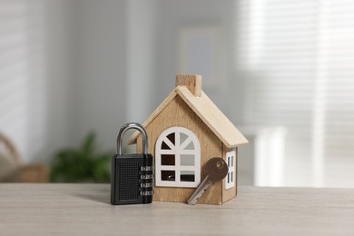 Photo of Home security. House model with key and padlock on wooden table indoors