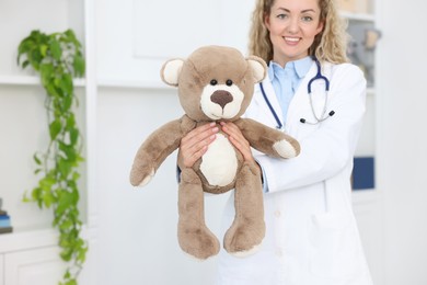 Photo of Pediatrician with toy bear in hospital, selective focus. Space for text