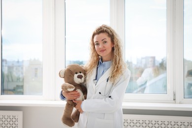 Photo of Pediatrician with toy bear near window in hospital