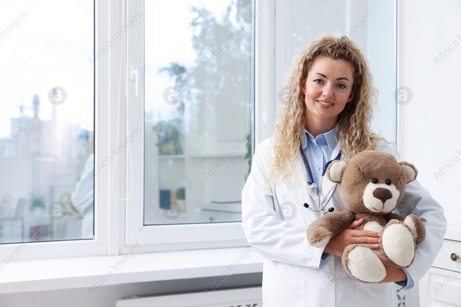 Pediatrician with toy bear near window in hospital. Space for text Photo of Pediatrician with toy bear near window in hospital. Space for text