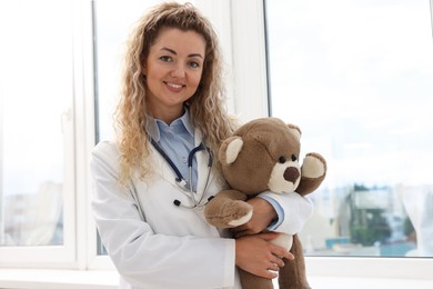 Photo of Pediatrician with toy bear near window in hospital