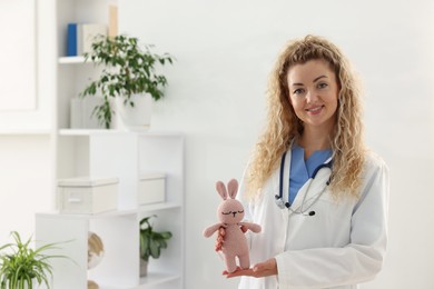 Photo of Professional pediatrician with toy bunny in hospital. Space for text