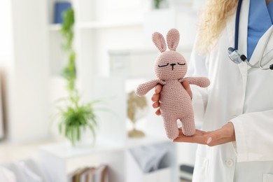 Photo of Professional pediatrician with toy bunny in hospital, closeup. Space for text