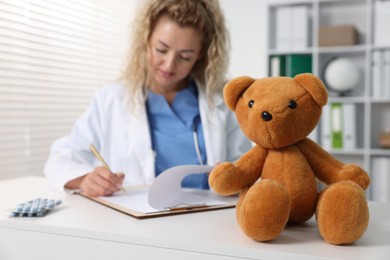 Photo of Pediatrician working at desk and toy bear in hospital, selective focus