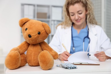 Photo of Pediatrician working at desk and toy bear in hospital, selective focus