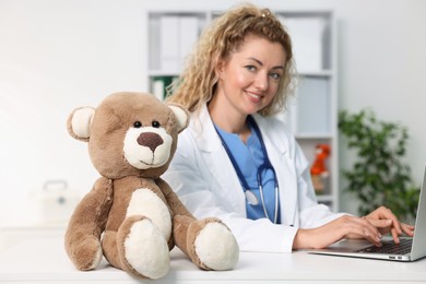 Photo of Pediatrician working at desk and toy bear in hospital, selective focus