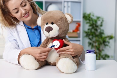 Photo of Pediatrician checking heartbeat of toy bear at desk in hospital
