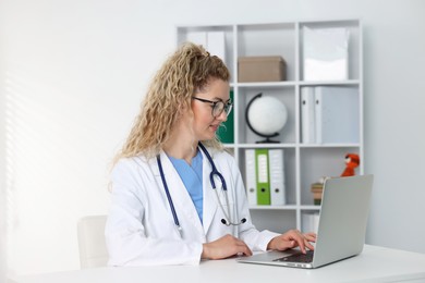 Photo of Professional pediatrician working on laptop at desk in clinic