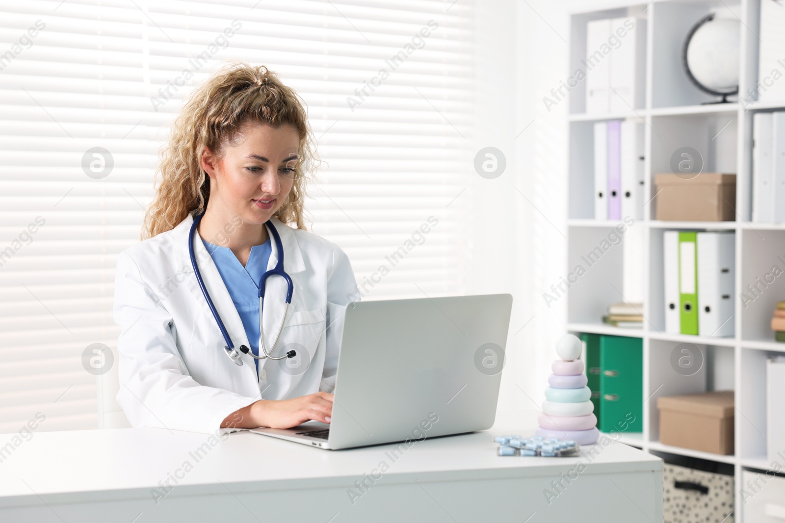 Professional pediatrician working on laptop at desk in clinic Photo of Professional pediatrician working on laptop at desk in clinic