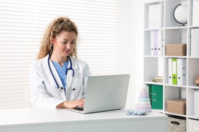 Photo of Professional pediatrician working on laptop at desk in clinic