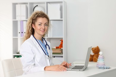 Photo of Professional pediatrician working on laptop at desk in clinic