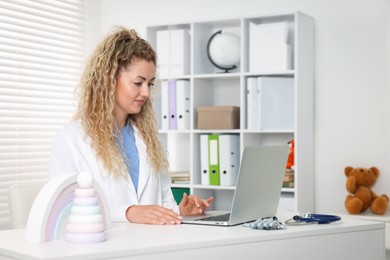 Photo of Professional pediatrician working on laptop at desk in clinic