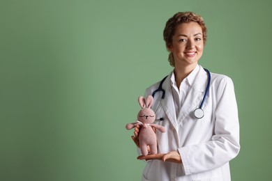 Photo of Professional pediatrician with toy bunny on olive background. Space for text