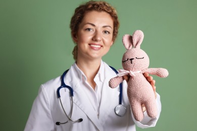 Photo of Professional pediatrician with toy bunny on olive background, selective focus