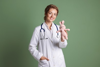 Photo of Professional pediatrician with toy bunny on olive background