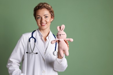 Photo of Professional pediatrician with toy bunny on olive background. Space for text
