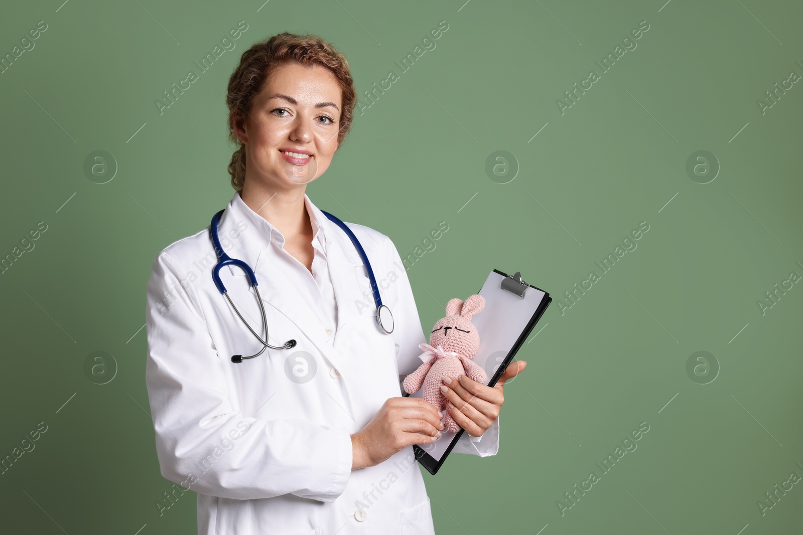 Professional pediatrician with toy bunny and clipboard on olive background. Space for text Photo of Professional pediatrician with toy bunny and clipboard on olive background. Space for text