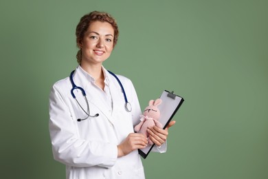 Photo of Professional pediatrician with toy bunny and clipboard on olive background. Space for text