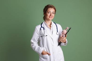 Photo of Professional pediatrician with toy bunny and clipboard on olive background