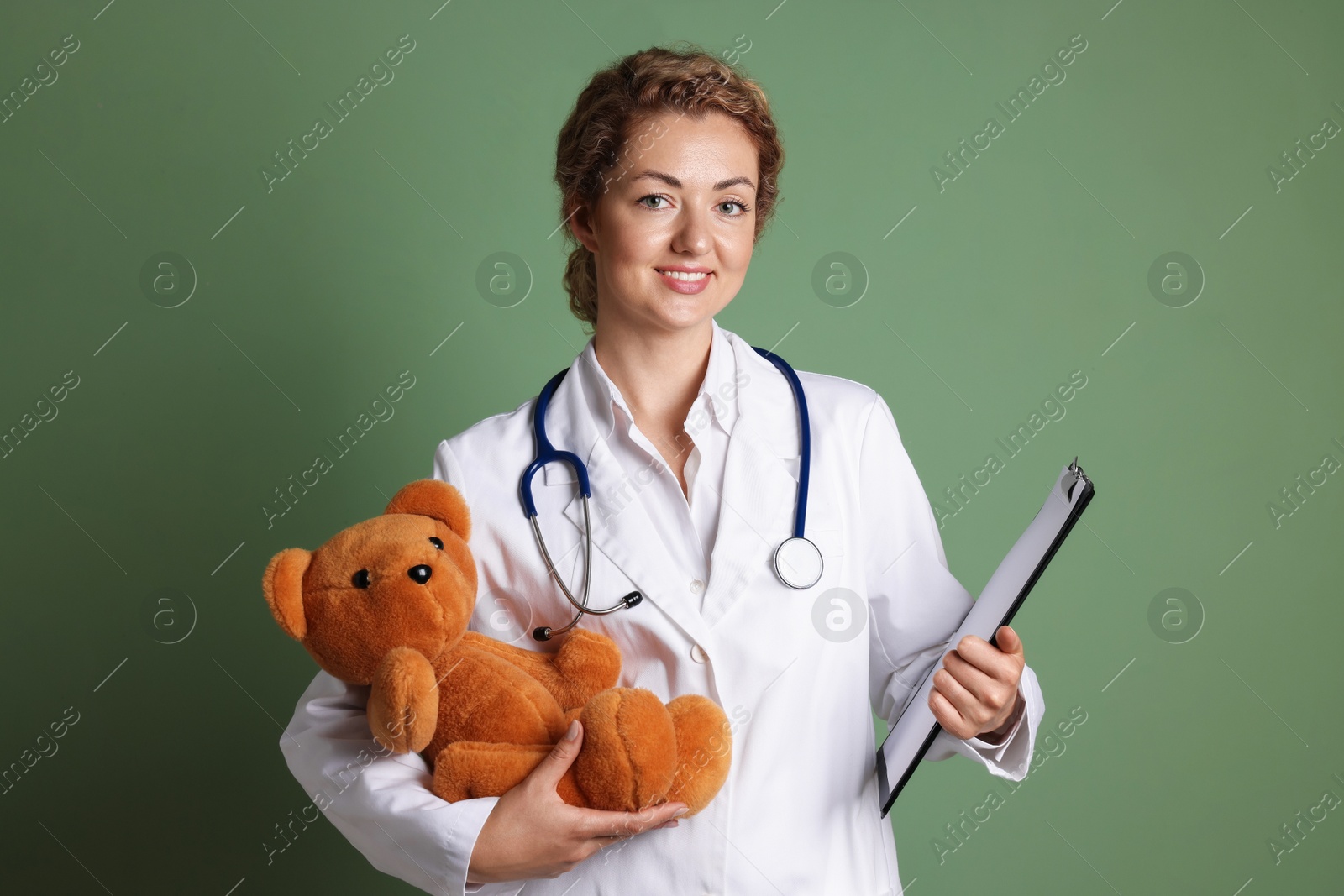 Pediatrician with toy bear and clipboard on olive background Photo of Pediatrician with toy bear and clipboard on olive background