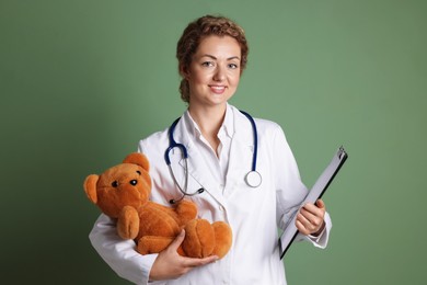 Photo of Pediatrician with toy bear and clipboard on olive background