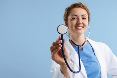 Photo of Professional pediatrician with stethoscope on light blue background, selective focus. Space for text