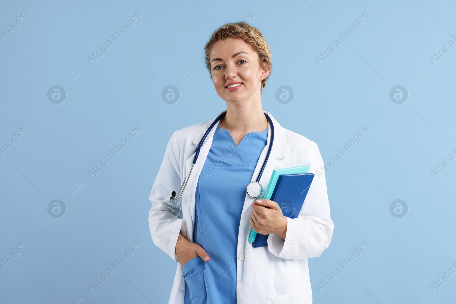 Portrait of professional pediatrician with stethoscope and notebooks on light blue background Photo of Portrait of professional pediatrician with stethoscope and notebooks on light blue background