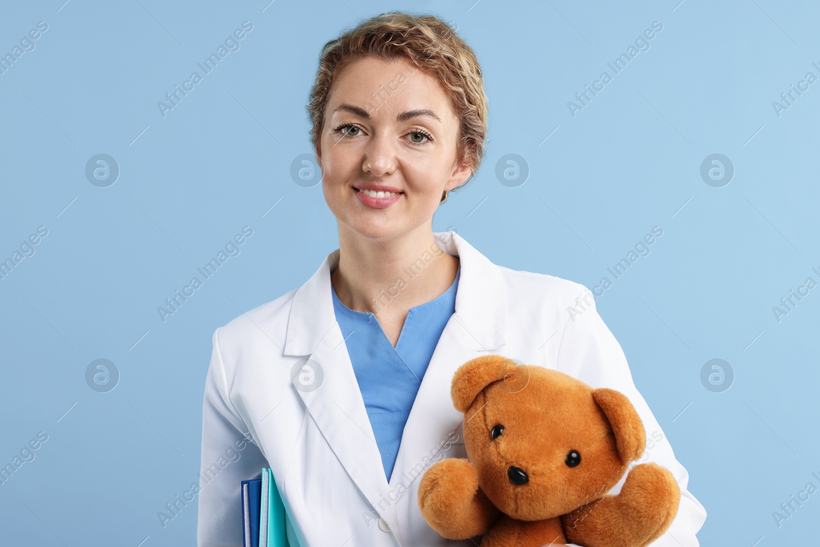 Pediatrician with toy bear on light blue background Photo of Pediatrician with toy bear on light blue background
