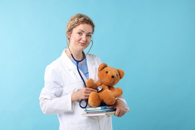 Photo of Pediatrician with notebooks checking heartbeat of toy bear on light blue background
