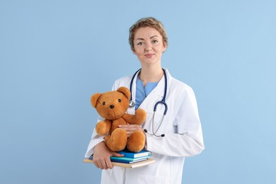 Photo of Pediatrician with toy bear and notebooks on light blue background