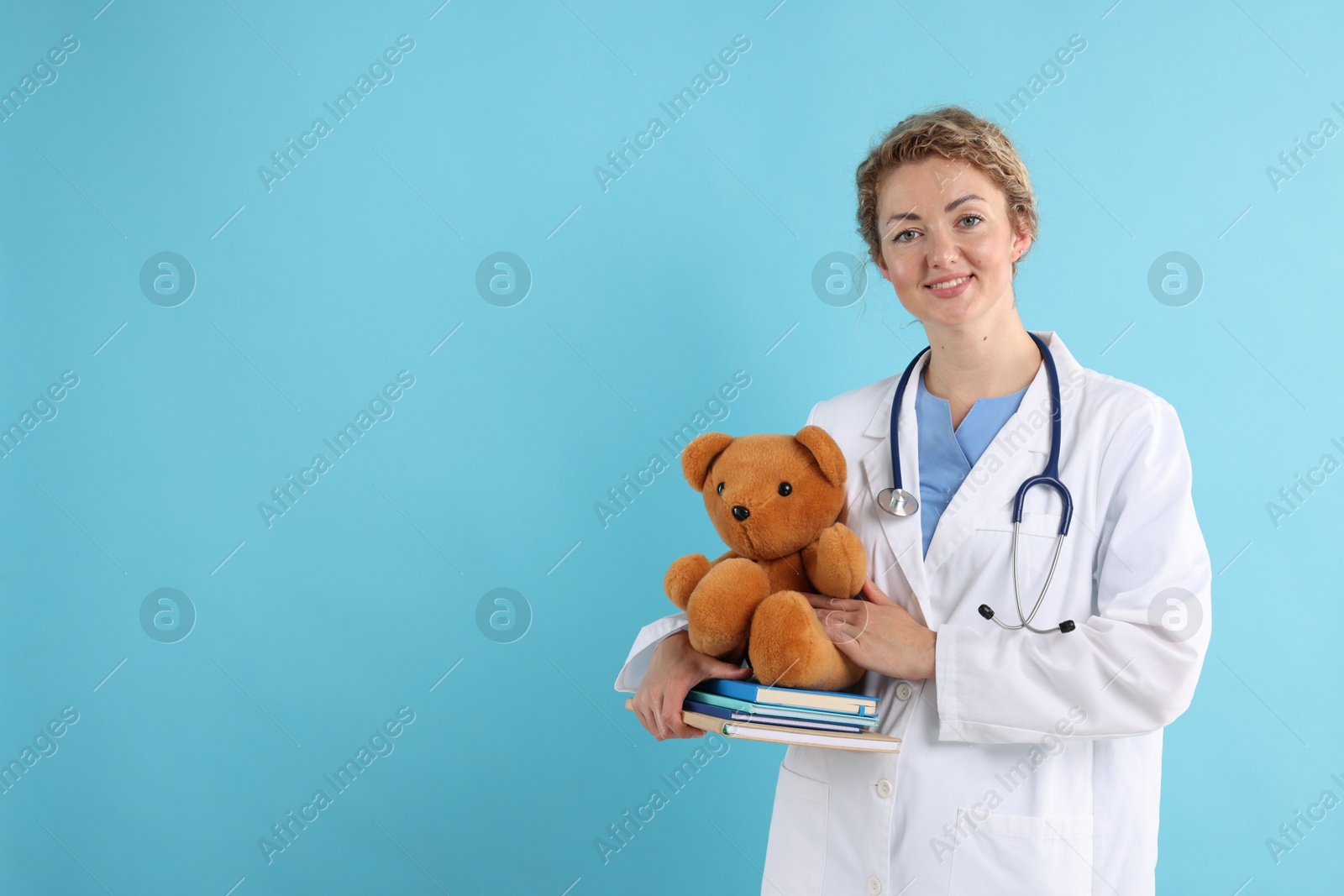 Pediatrician with toy bear and notebooks on light blue background. Space for text Photo of Pediatrician with toy bear and notebooks on light blue background. Space for text