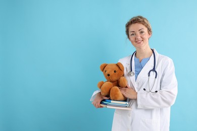 Photo of Pediatrician with toy bear and notebooks on light blue background. Space for text