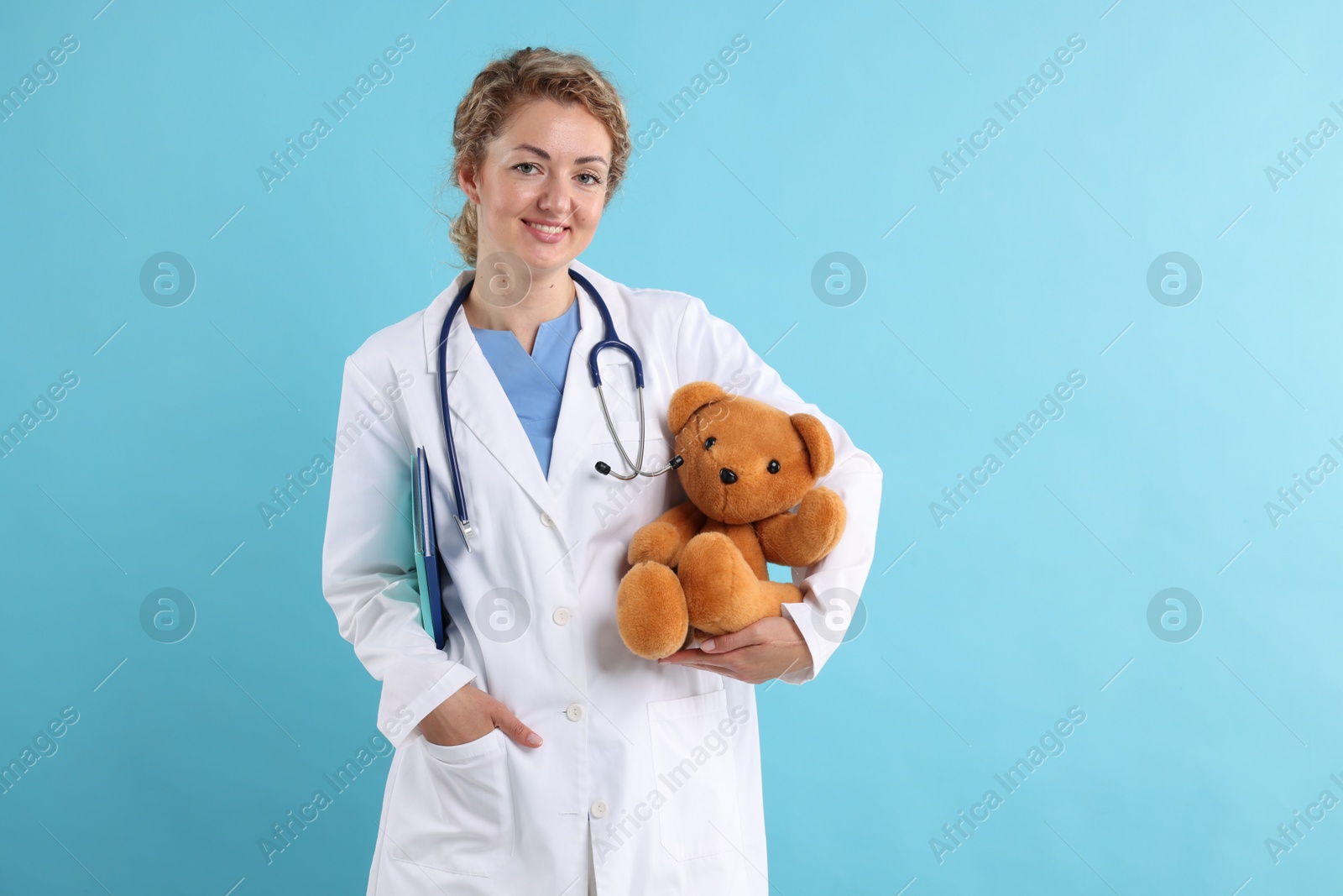 Pediatrician with toy bear and notebooks on light blue background. Space for text Photo of Pediatrician with toy bear and notebooks on light blue background. Space for text