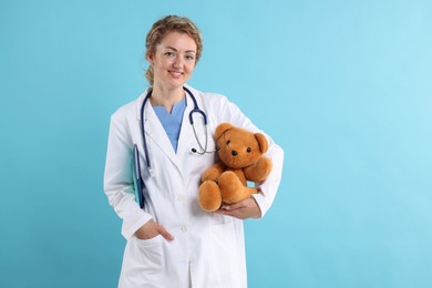 Photo of Pediatrician with toy bear and notebooks on light blue background. Space for text