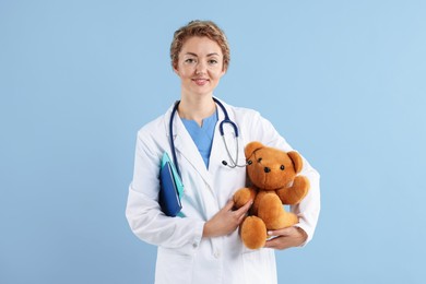Photo of Pediatrician with toy bear and notebooks on light blue background