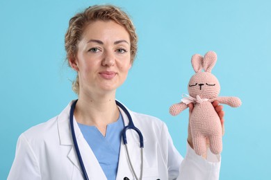 Photo of Professional pediatrician with toy bunny on light blue background