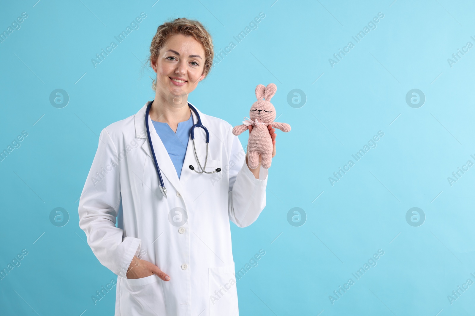 Professional pediatrician with toy bunny on light blue background. Space for text Photo of Professional pediatrician with toy bunny on light blue background. Space for text