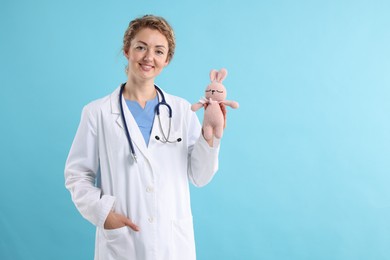 Photo of Professional pediatrician with toy bunny on light blue background. Space for text