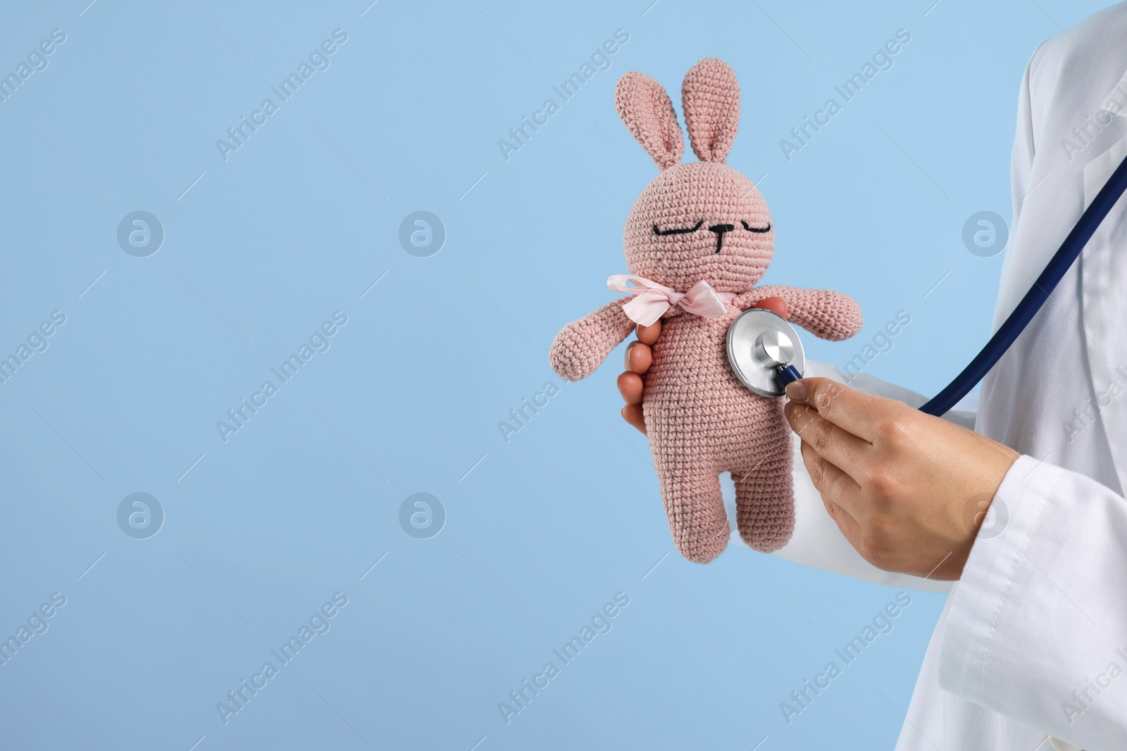 Professional pediatrician checking heartbeat of toy bunny on light blue background, closeup. Space for text Photo of Professional pediatrician checking heartbeat of toy bunny on light blue background, closeup. Space for text