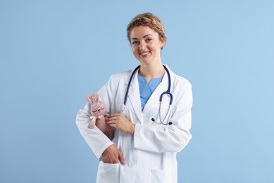 Photo of Professional pediatrician with toy bunny on light blue background