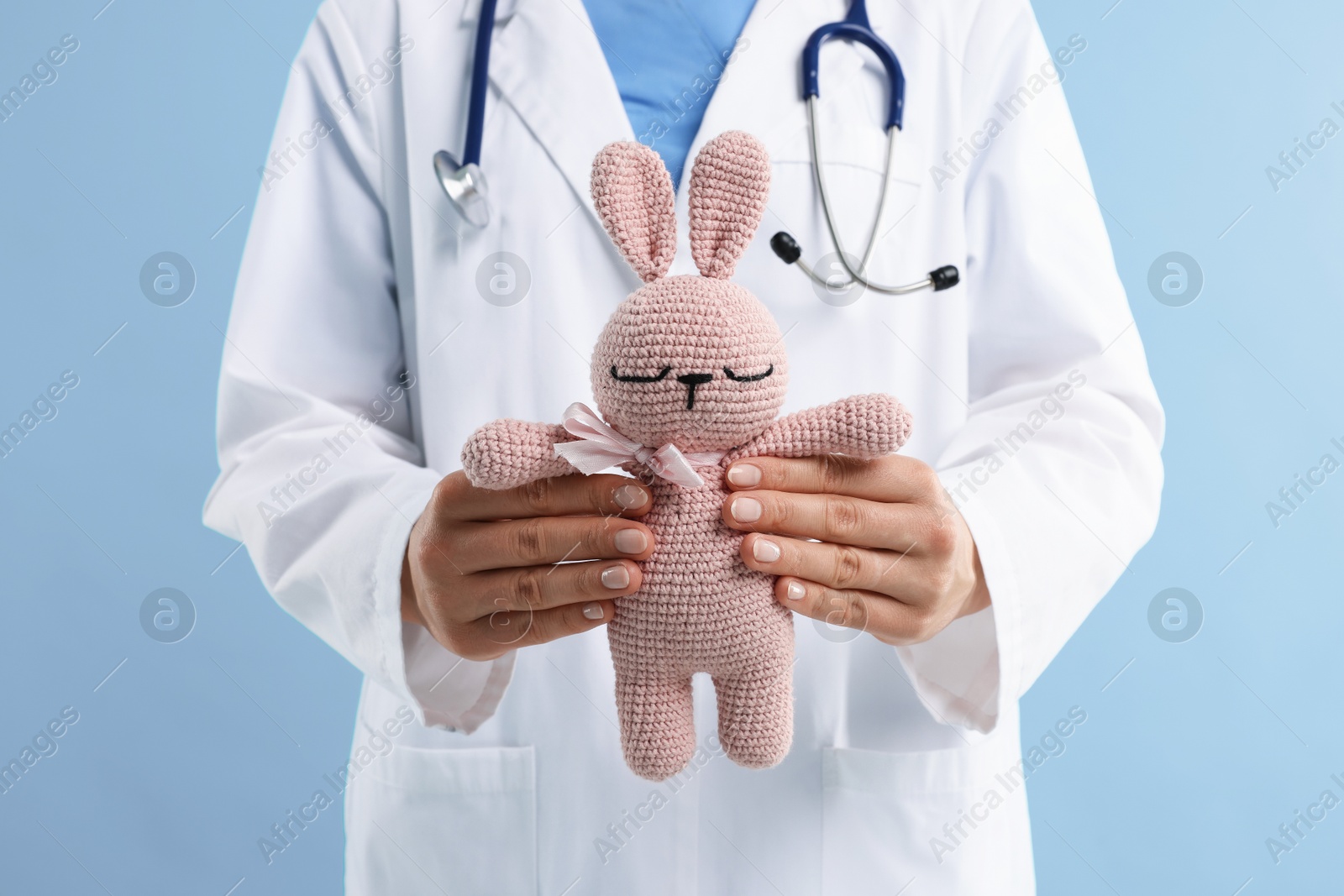 Professional pediatrician with toy bunny on light blue background, closeup Photo of Professional pediatrician with toy bunny on light blue background, closeup