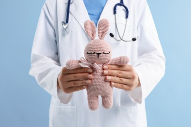 Photo of Professional pediatrician with toy bunny on light blue background, closeup