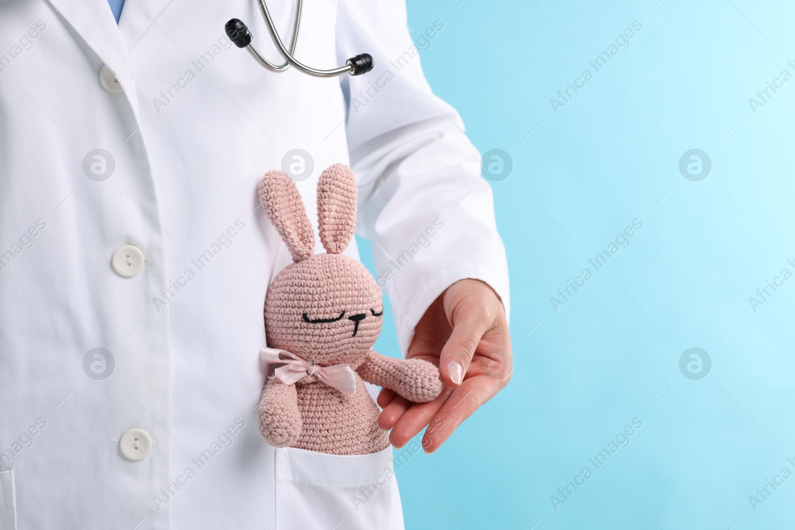 Professional pediatrician with toy bunny in pocket on light blue background, closeup. Space for text Photo of Professional pediatrician with toy bunny in pocket on light blue background, closeup. Space for text