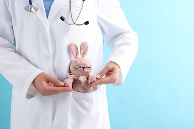 Photo of Professional pediatrician with toy bunny in pocket on light blue background, closeup. Space for text