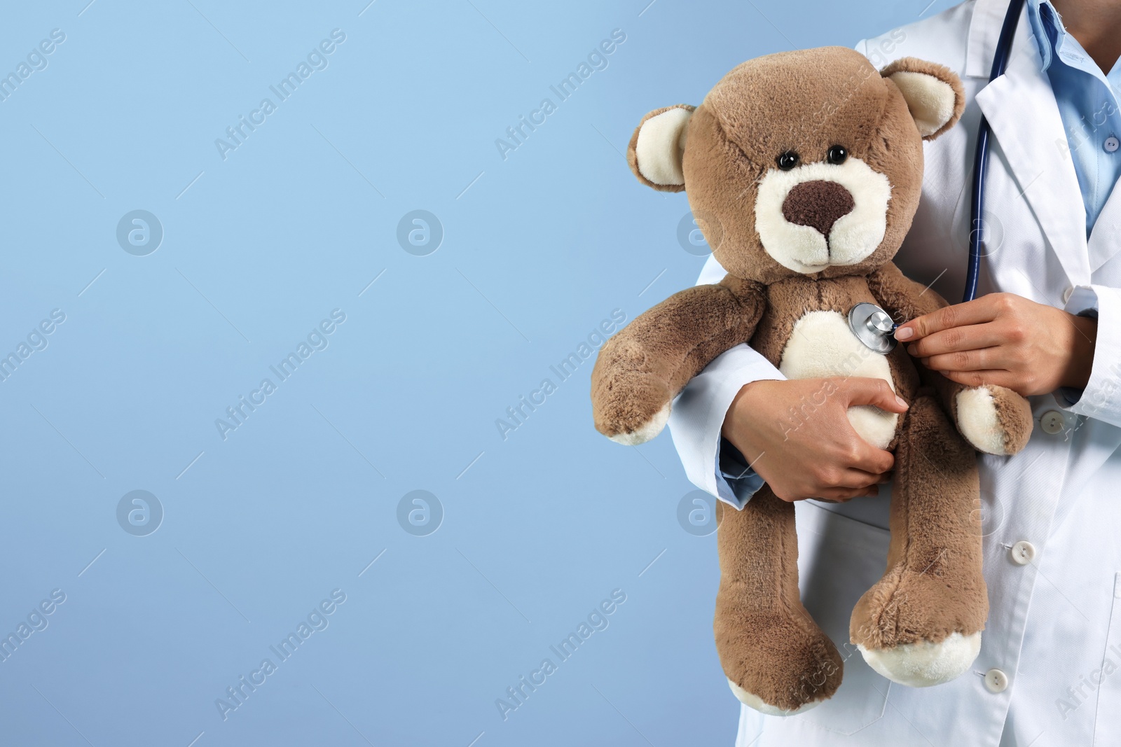 Pediatrician checking heartbeat of toy bear on light blue background, closeup. Space for text Photo of Pediatrician checking heartbeat of toy bear on light blue background, closeup. Space for text