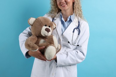 Photo of Pediatrician with toy bear on light blue background, closeup